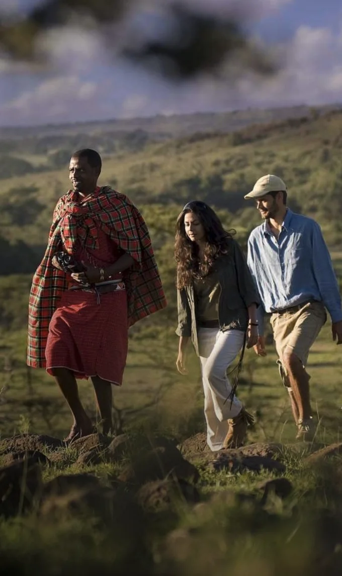 Maasai guide walking two guests across the green highlands of Kenya
