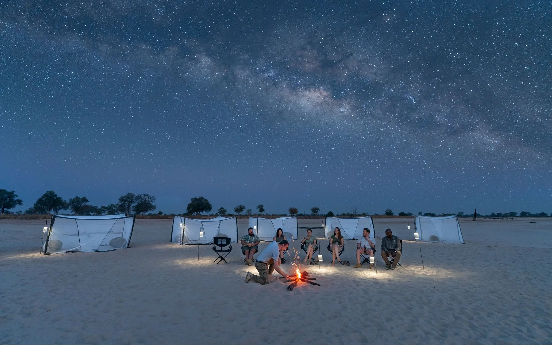 Guests around a campfire at a fly camp on an open sandbank under a sky full of stars