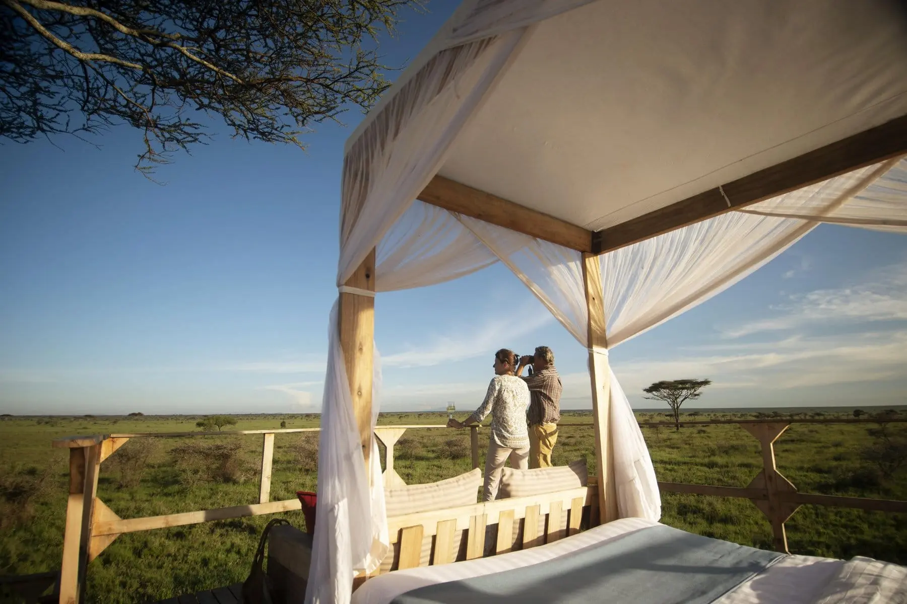 Guest standing at a four-poster star bed looking over the Serengeti plains at dusk
