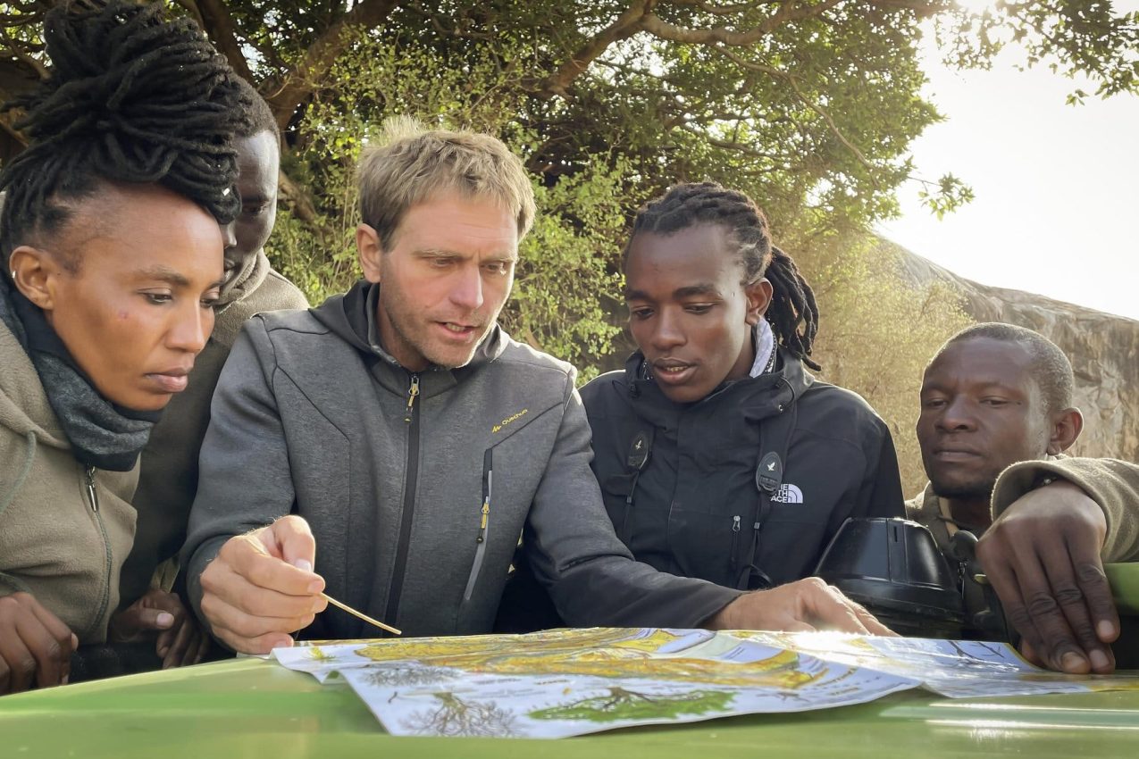 Guides tracing a route across a Serengeti map on a vehicle bonnet