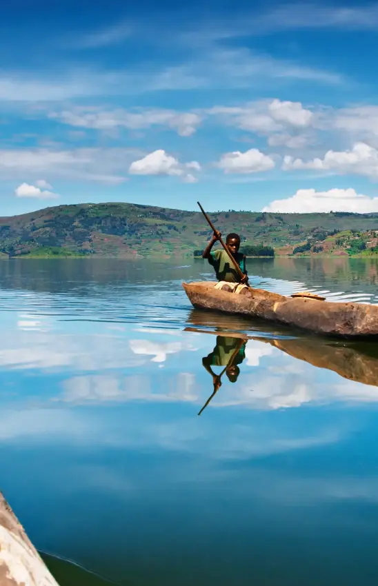 Fisherman poling wooden canoe across calm lake waters