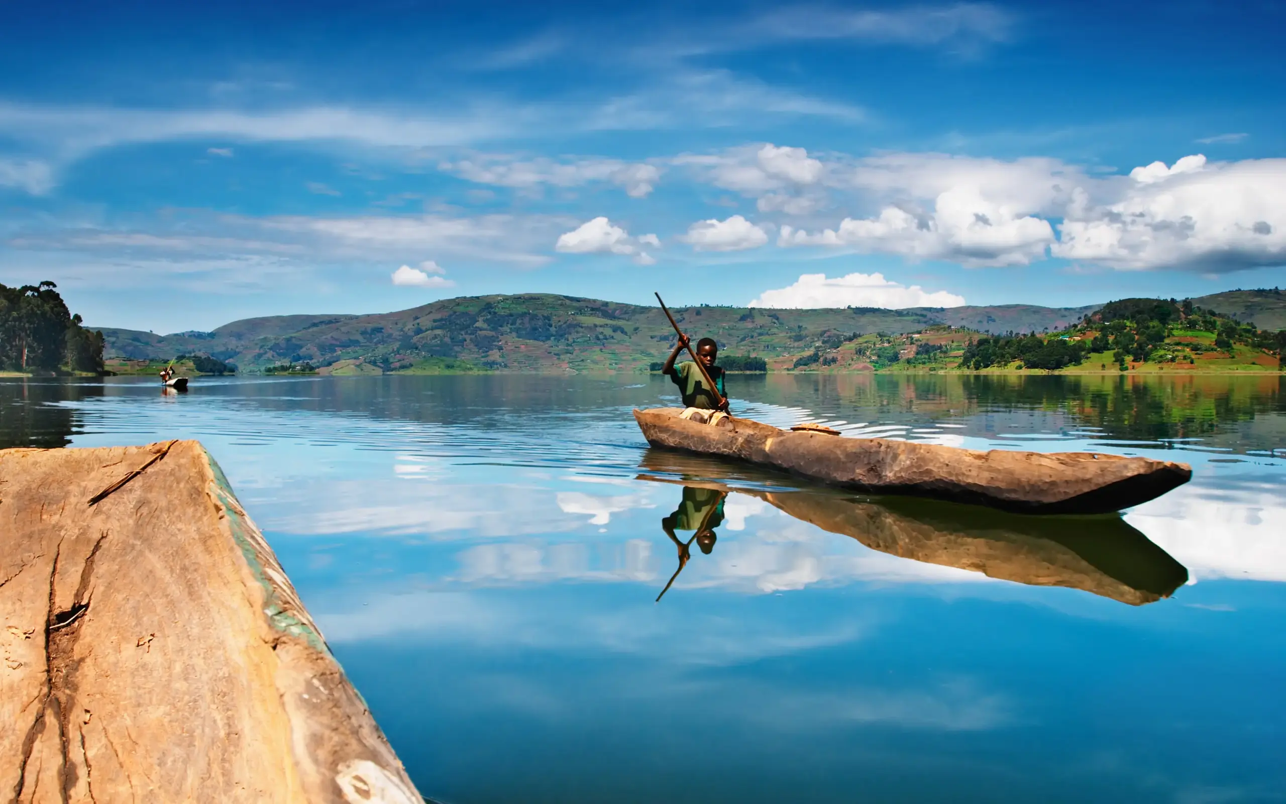 Fisherman poling wooden canoe across calm lake waters