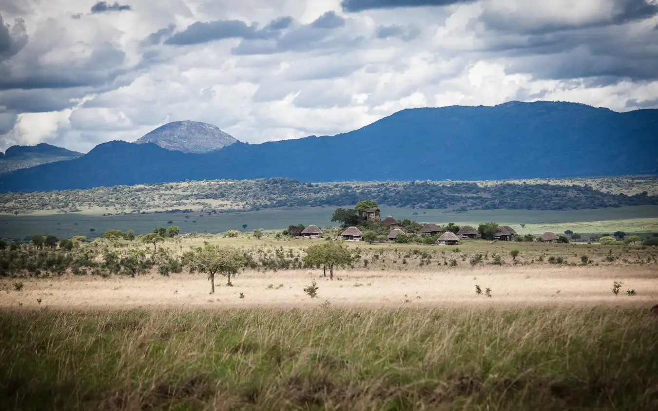 Savanna grassland with distant mountains and scattered buildings, Apoka Safari Lodge, Kidepo Valley, Uganda