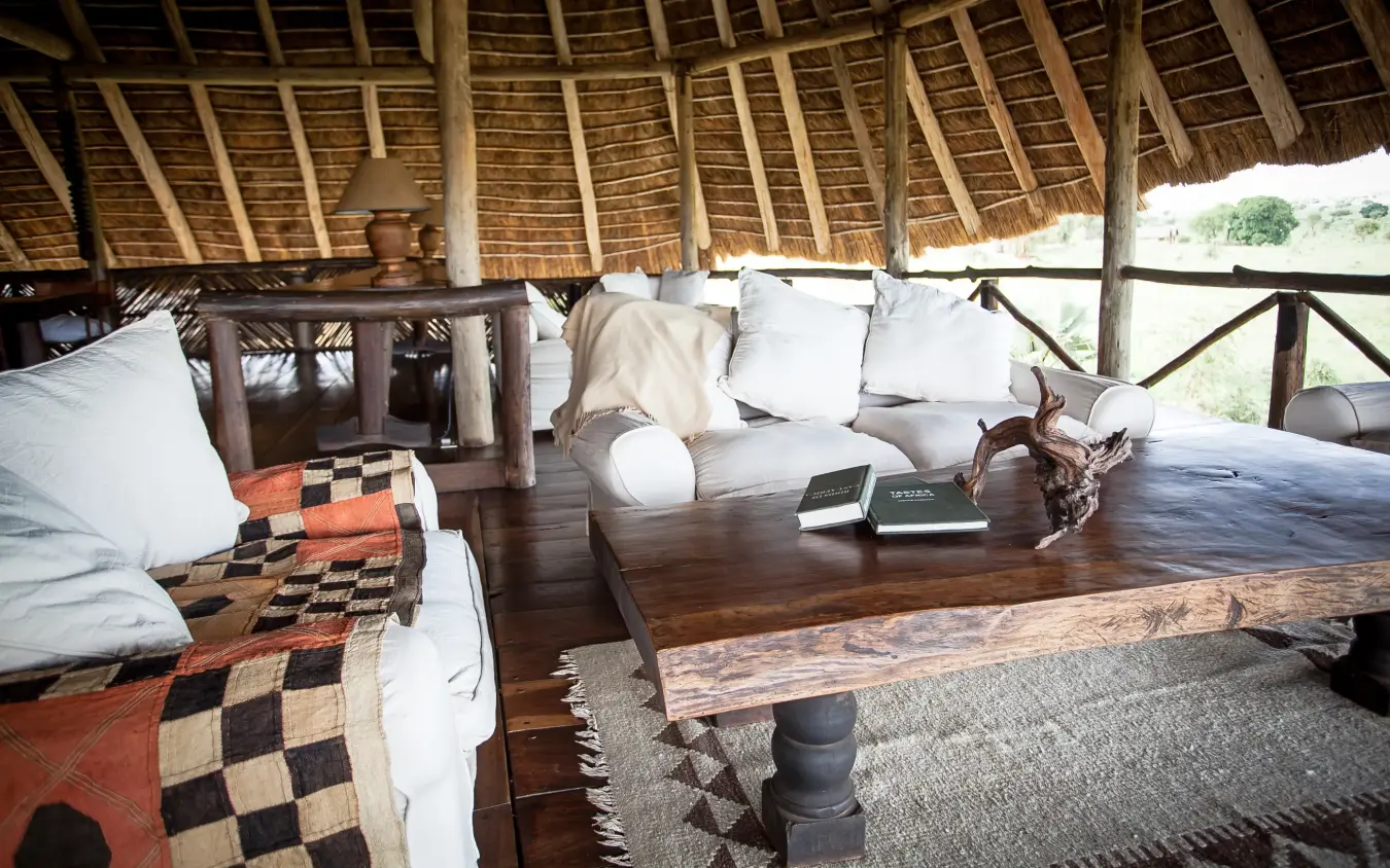 Thatched roof lounge with wooden furnishings and white cushions, Apoka Safari Lodge, Kidepo Valley, Uganda