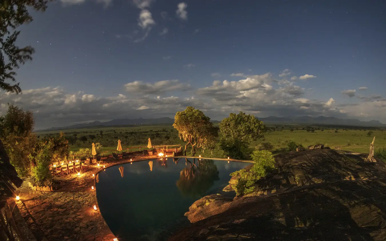 Illuminated infinity pool overlooking African savanna at dusk, Apoka Safari Lodge, Kidepo Valley, Uganda