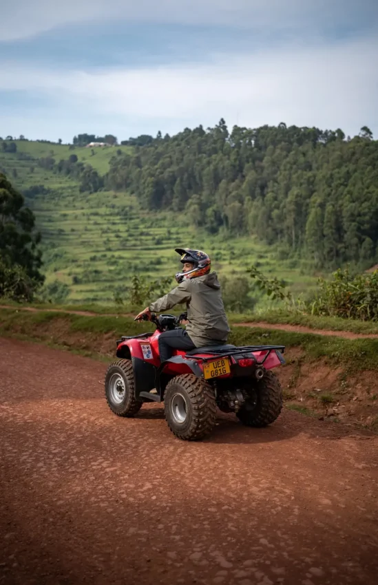 Guest riding red ATV on rural dirt road with forested hills, Lake Bunyonyi, Uganda