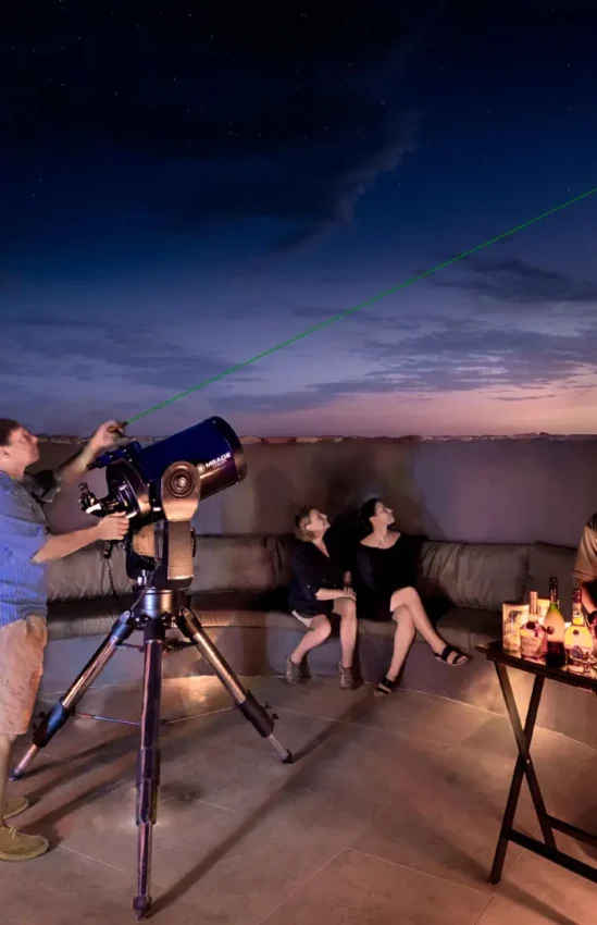 Guests stargazing on rooftop deck at dusk with telescope, Sossusvlei Desert Lodge, NamibRand Private Reserve, Namibia