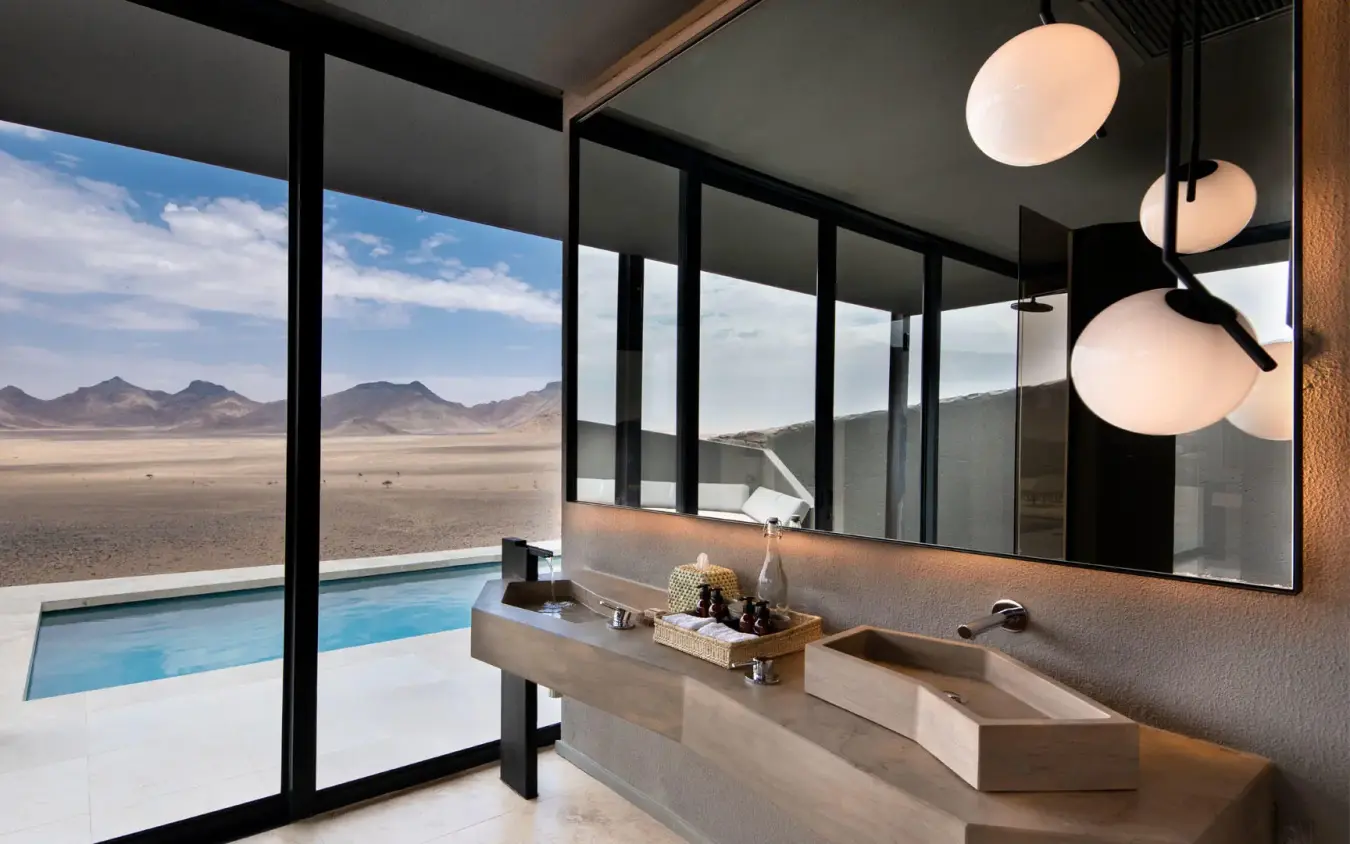 Modern bathroom with vanity overlooking desert landscape and pool, Sossusvlei Desert Lodge, NamibRand Private Reserve, Namibia