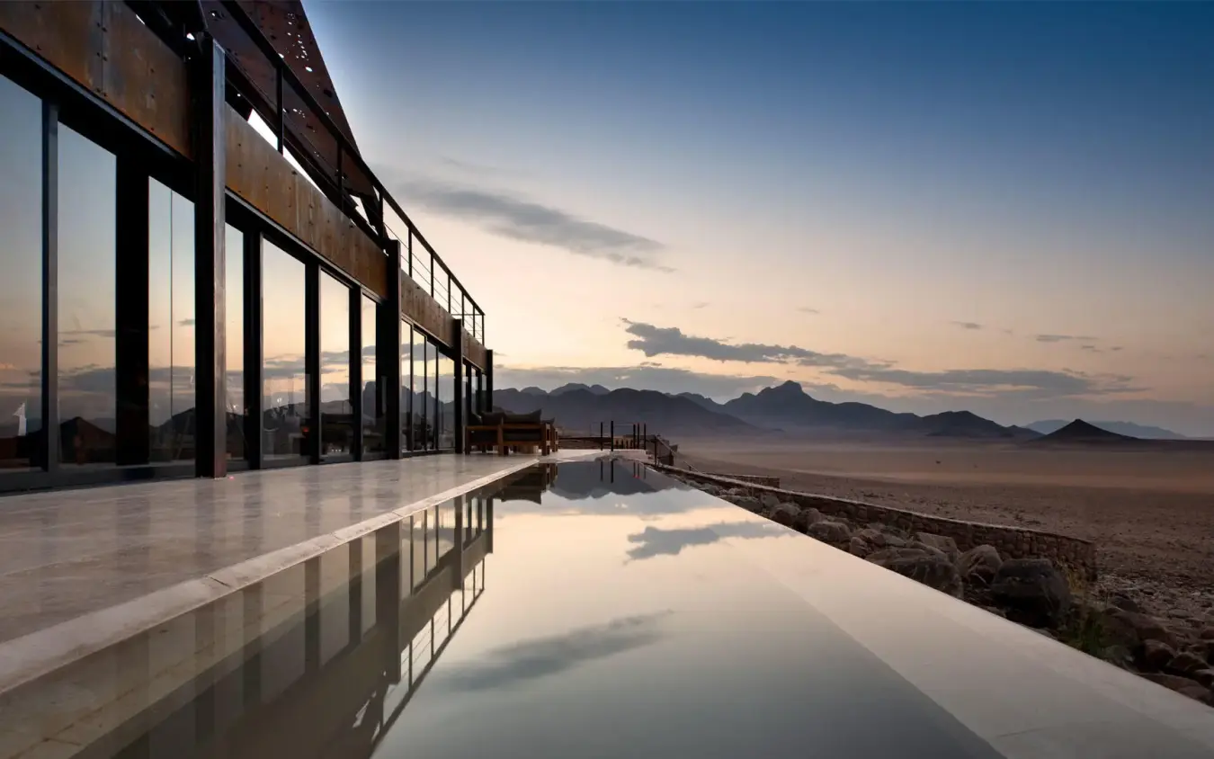 Infinity pool overlooking desert landscape at sunset, Sossusvlei Desert Lodge, NamibRand Private Reserve, Namibia