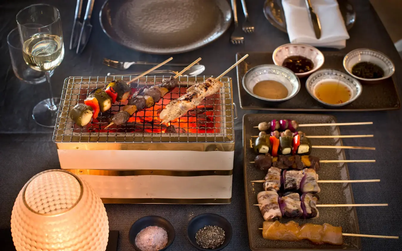 Table setting with grilled meat skewers and vegetables on tabletop grill, Sossusvlei Desert Lodge, NamibRand Private Reserve, Namibia