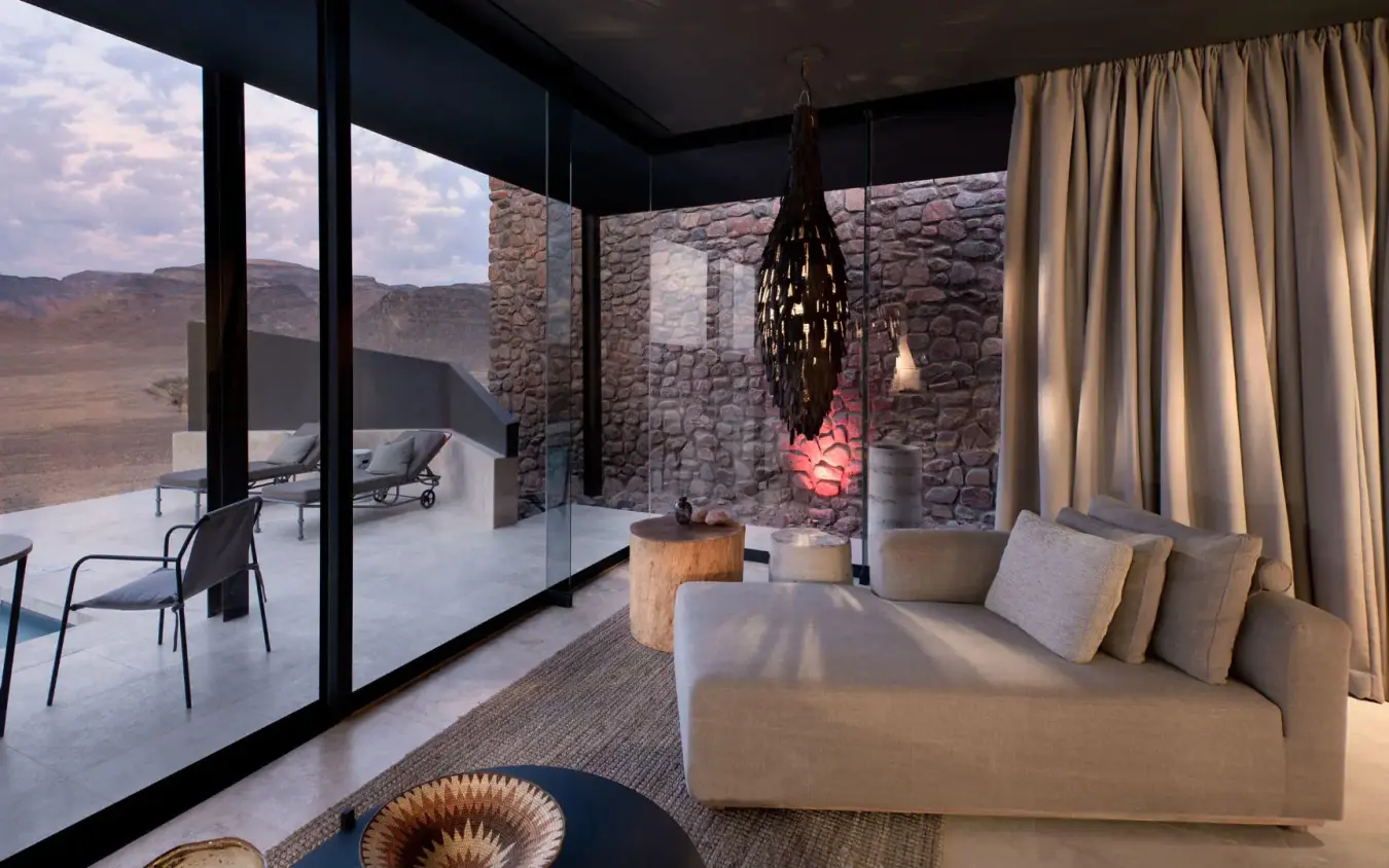 Modern bedroom with stone wall and desert landscape views, Sossusvlei Desert Lodge, NamibRand Private Reserve, Namibia