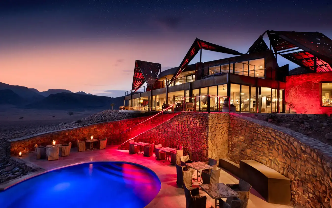 Illuminated resort pool at dusk with desert mountains, Sossusvlei Desert Lodge, NamibRand Private Reserve, Namibia