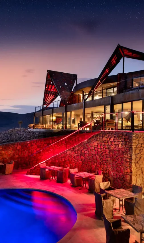 Illuminated resort pool at dusk with desert mountains, Sossusvlei Desert Lodge, NamibRand Private Reserve, Namibia