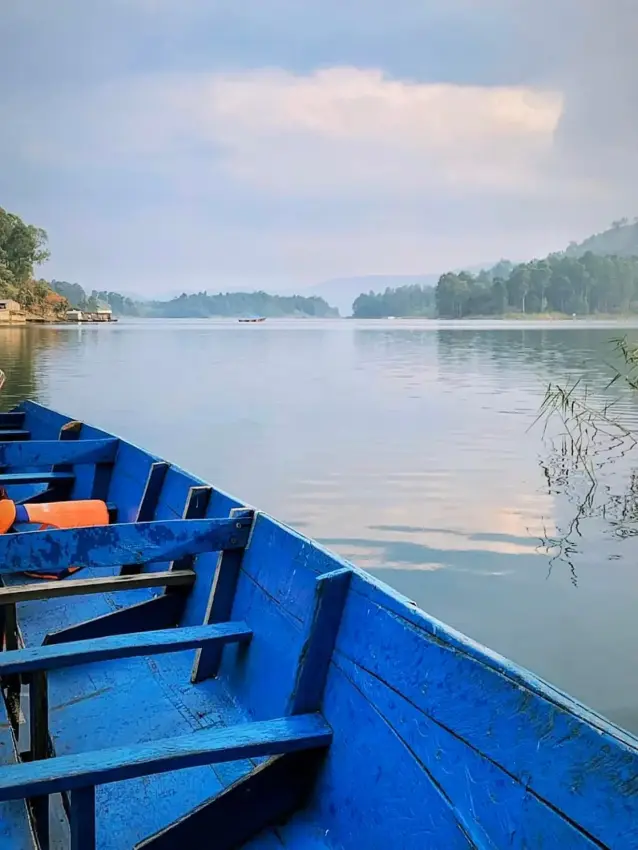 Blue wooden boat on calm lake with forested shoreline, Lake Bunyonyi, Uganda