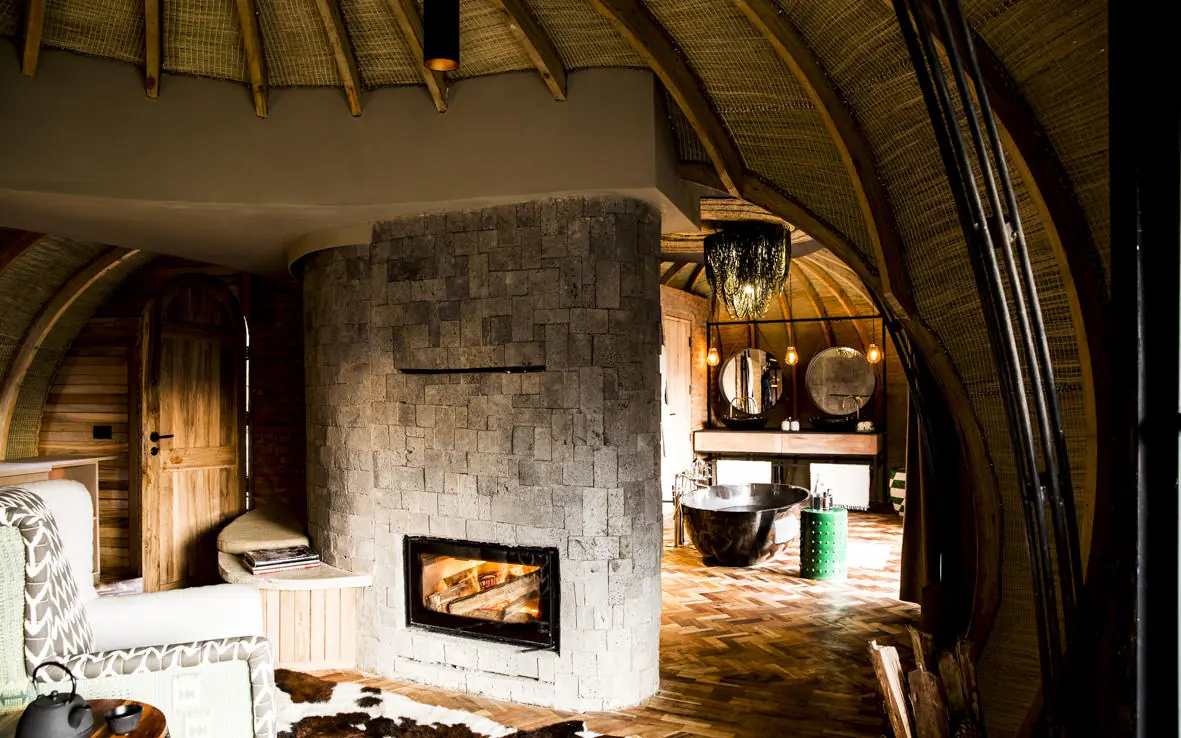 Interior of thatched-roof lodge with stone fireplace and seating, Bisate Lodge, Volcanoes National Park, Rwanda
