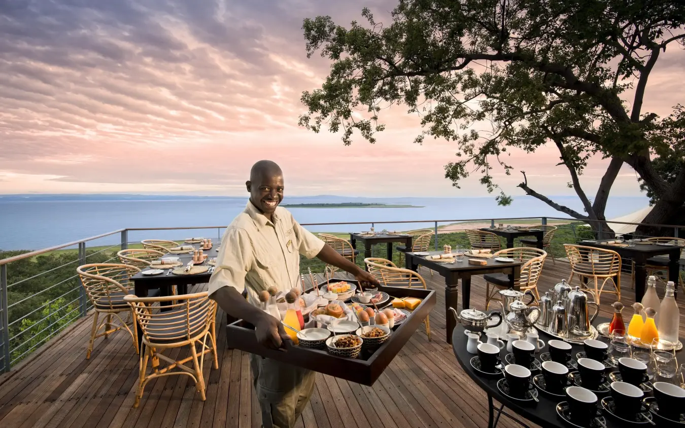 Server presenting breakfast on wooden deck overlooking water, Bumi Hills Safari Lodge, Matusadona National Park, Zimbabwe