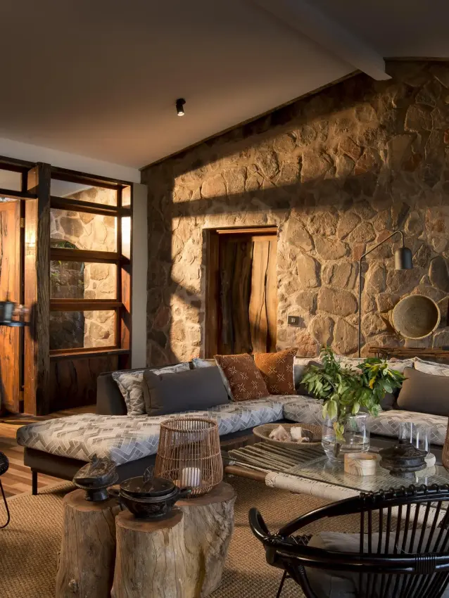 Stone-walled lounge with seating and glass doors at dusk, Bumi Hills Safari Lodge, Matusadona National Park, Zimbabwe