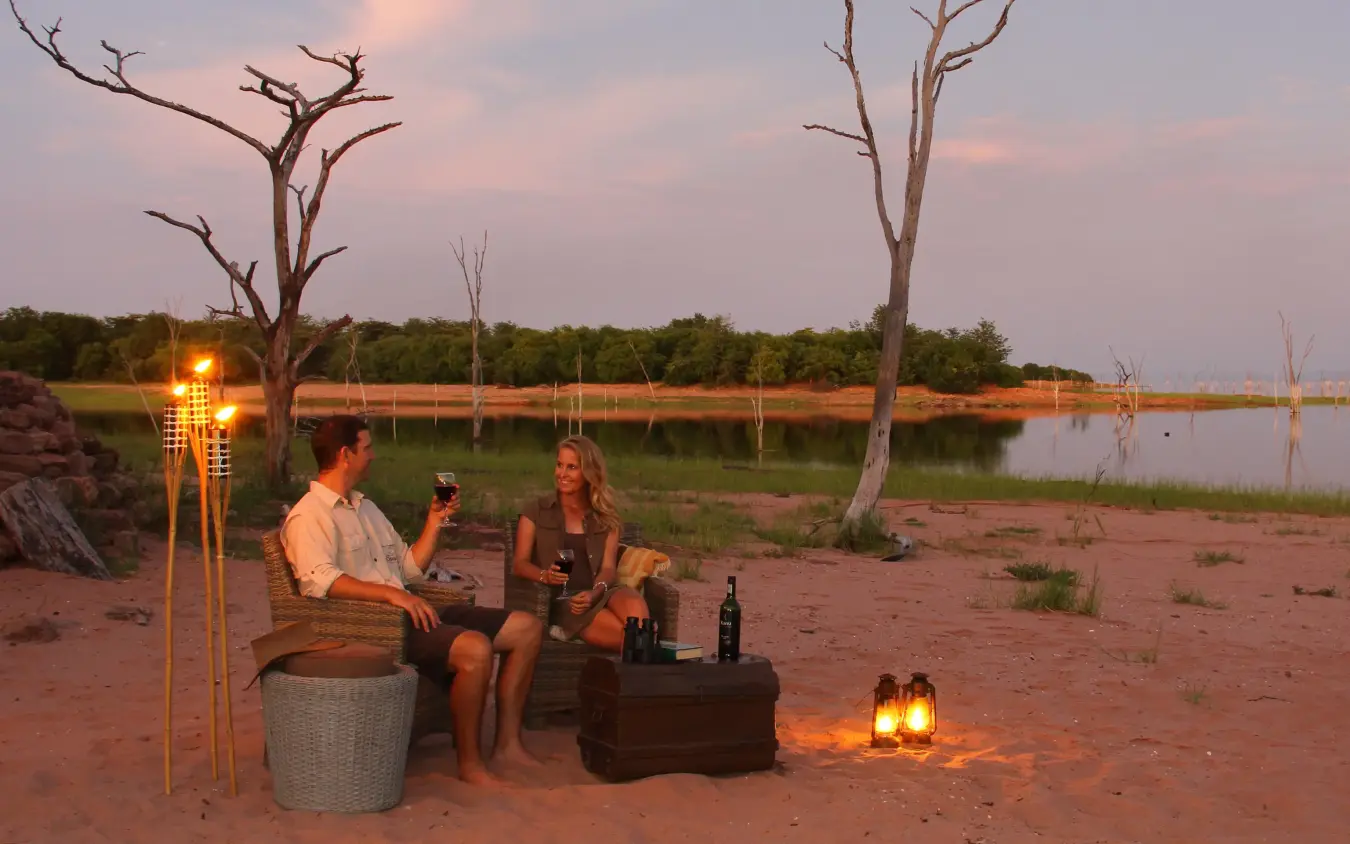 Guests enjoying evening drinks by waterside at sunset, Changa Safari Camp, Matusadona National Park, Zimbabwe