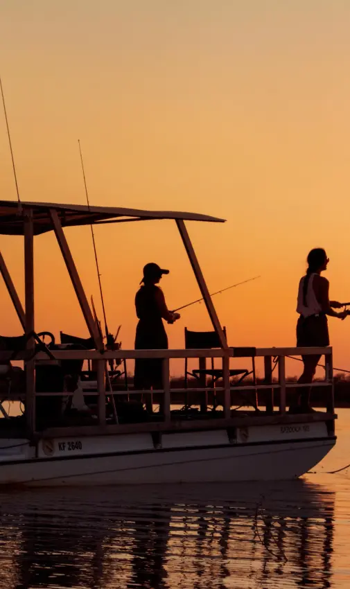 Fishermen silhouetted against sunset on shallow water boat, Changa Safari Camp, Matusadona National Park, Zimbabwe