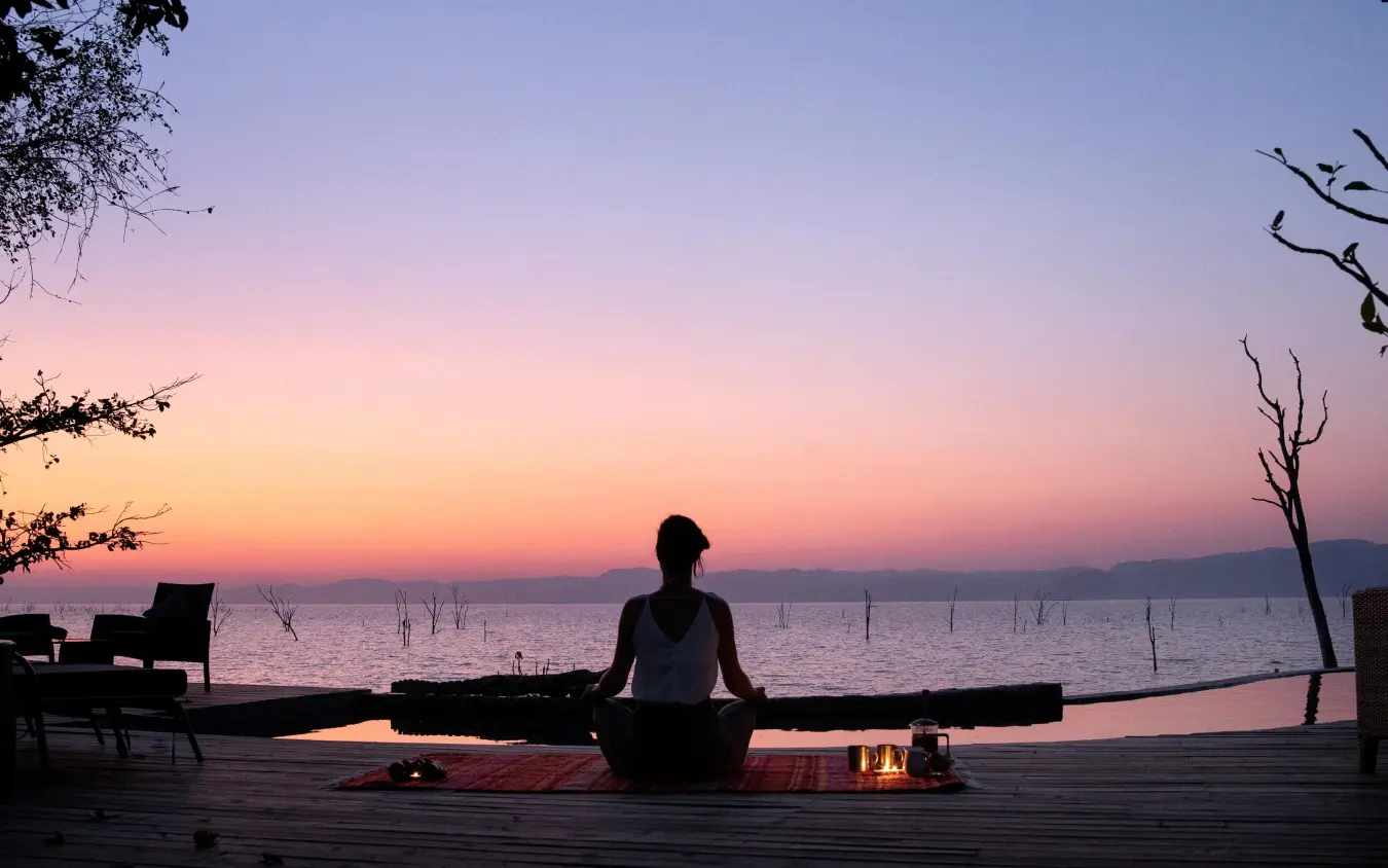 Person meditating on wooden deck at sunset by water, Changa Safari Camp, Matusadona National Park, Zimbabwe