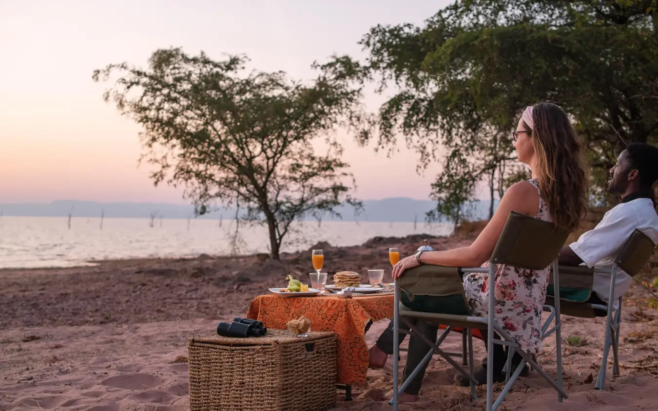 Couple dining on beach at sunset with water view, Changa Safari Camp, Matusadona National Park, Zimbabwe
