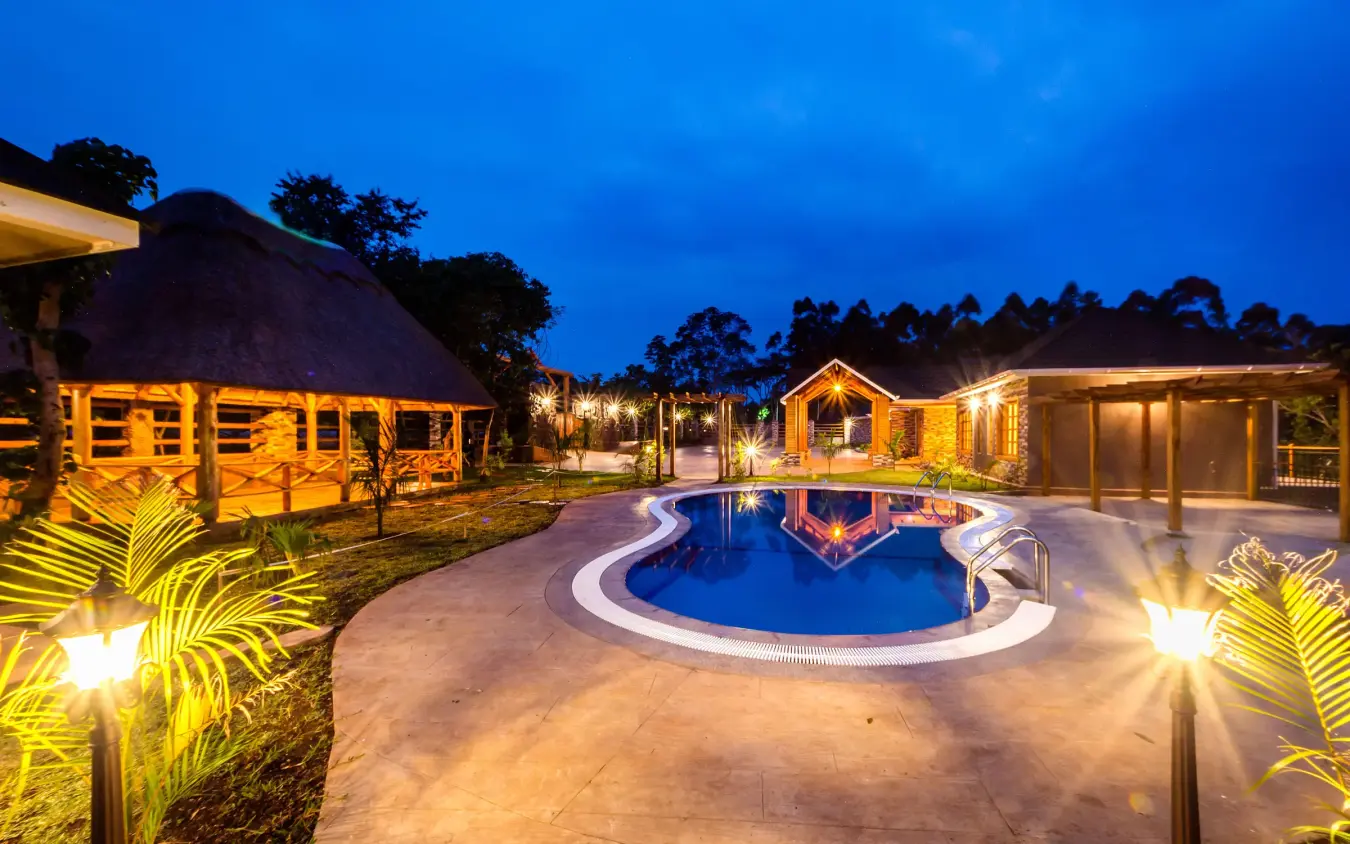 Illuminated resort pool with thatched lodge buildings at dusk, Chimpundu Lodge, Kibale Forest, Uganda