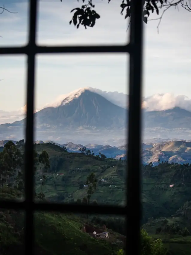 Snow-capped volcano viewed through window with green valleys, Clouds Mountain Gorilla Lodge, Bwindi Impenetrable Forest, Uganda