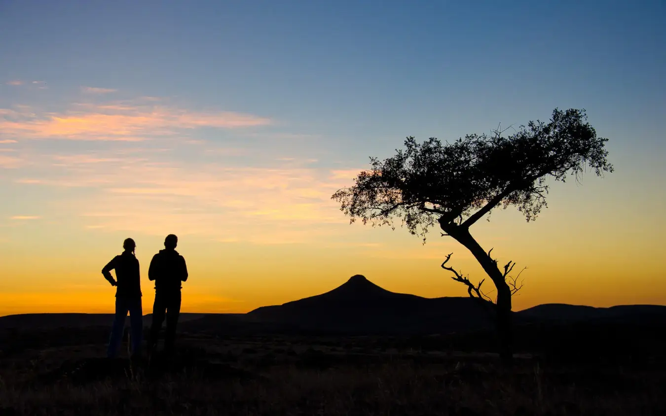 Two guests silhouetted at sunset watching landscape, Damaraland Camp, Damaraland, Namibia