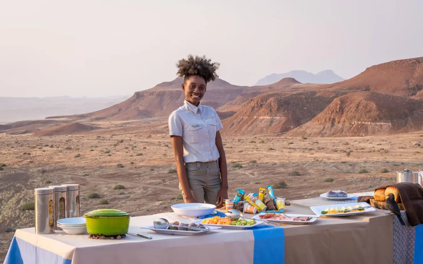 Staff member at outdoor dining table with desert landscape, Damaraland Camp, Damaraland, Namibia