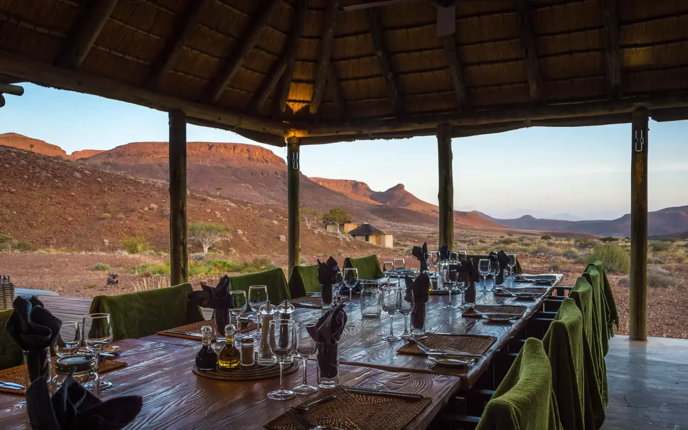 Long dining table set under thatched roof with mountain views, Damaraland Camp, Damaraland, Namibia