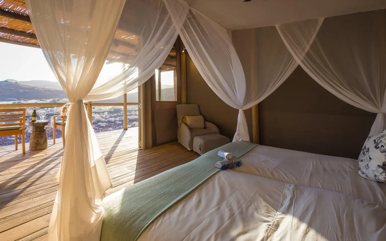 Bedroom with sheer curtains overlooking desert landscape, Damaraland Camp, Damaraland, Namibia