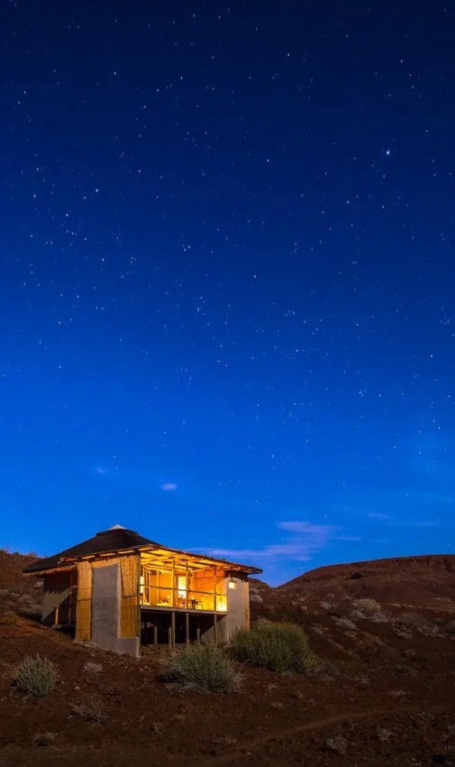 Illuminated lodge building on desert hillside at dusk, Damaraland Camp, Damaraland, Namibia