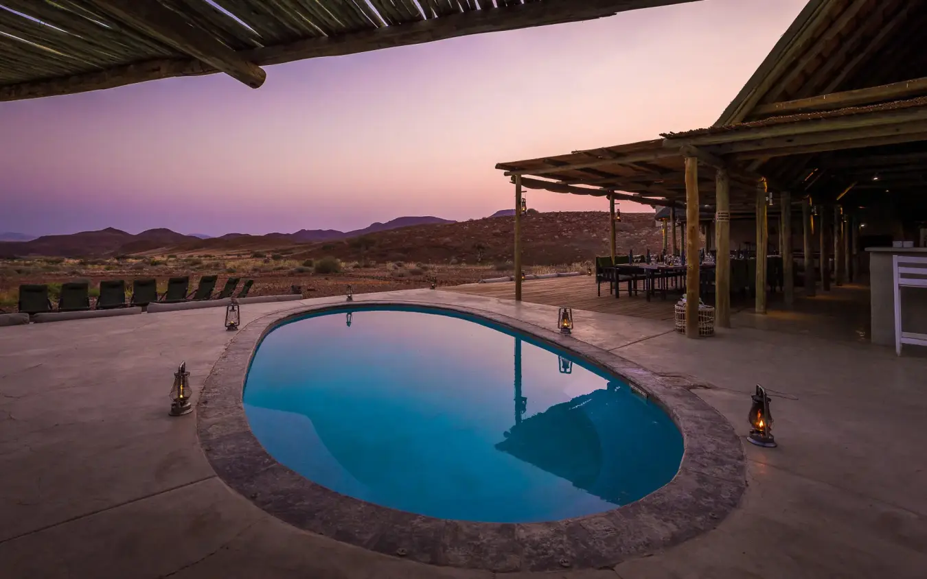 Illuminated pool at dusk with desert landscape beyond, Damaraland Camp, Damaraland, Namibia