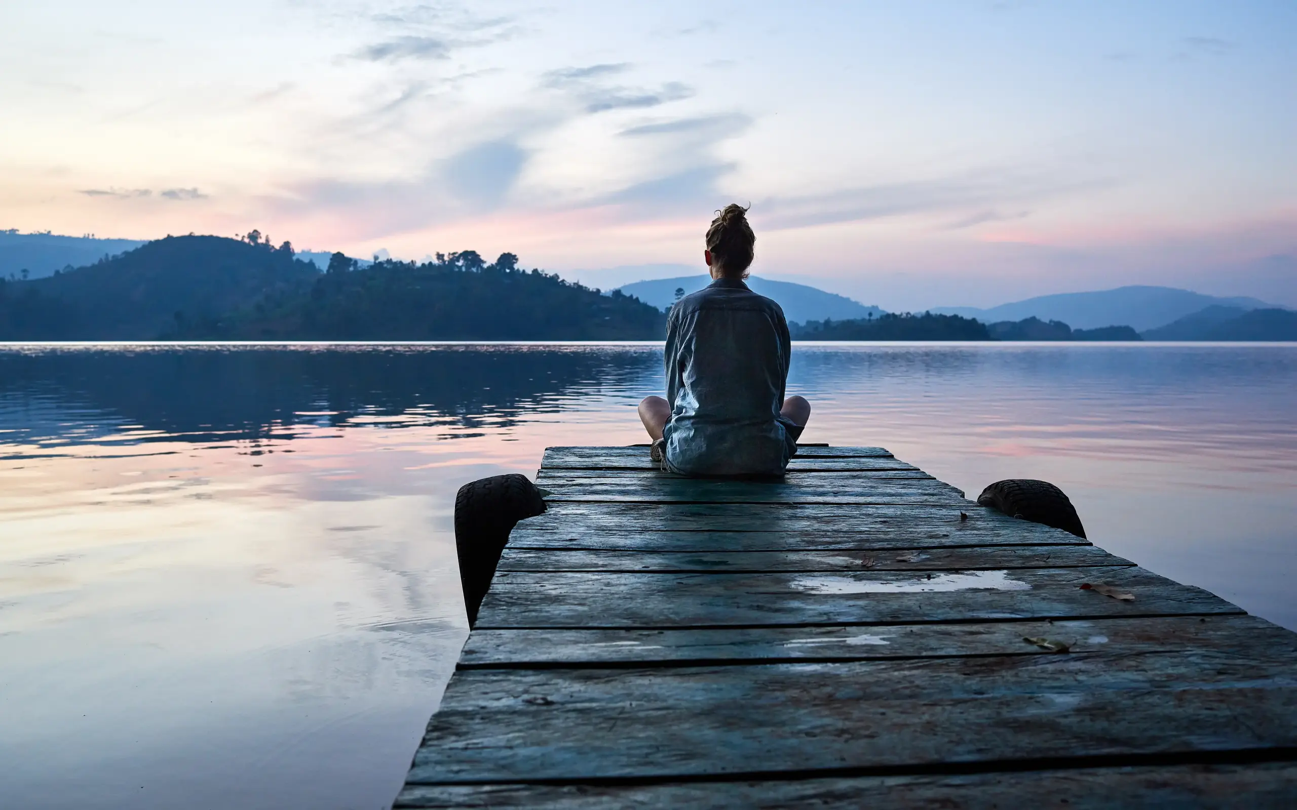 Person sitting on wooden dock overlooking calm lake at sunset