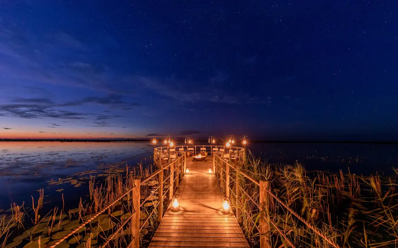 Illuminated wooden boardwalk extending into wetland at dusk, DumaTau, Linyanti Wildlife Reserve, Botswana