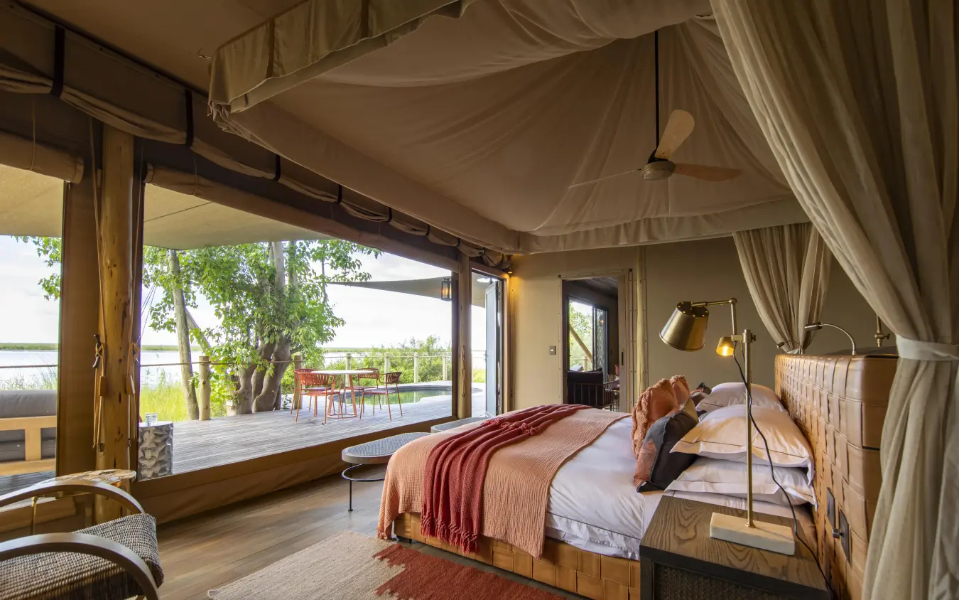 Bedroom with draped canopy overlooking waterfront deck and landscape, DumaTau, Linyanti Wildlife Reserve, Botswana