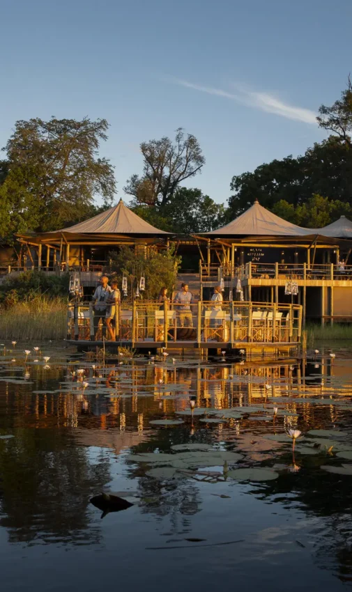 Waterfront lodge with thatched structures reflected in water, DumaTau, Linyanti Wildlife Reserve, Botswana