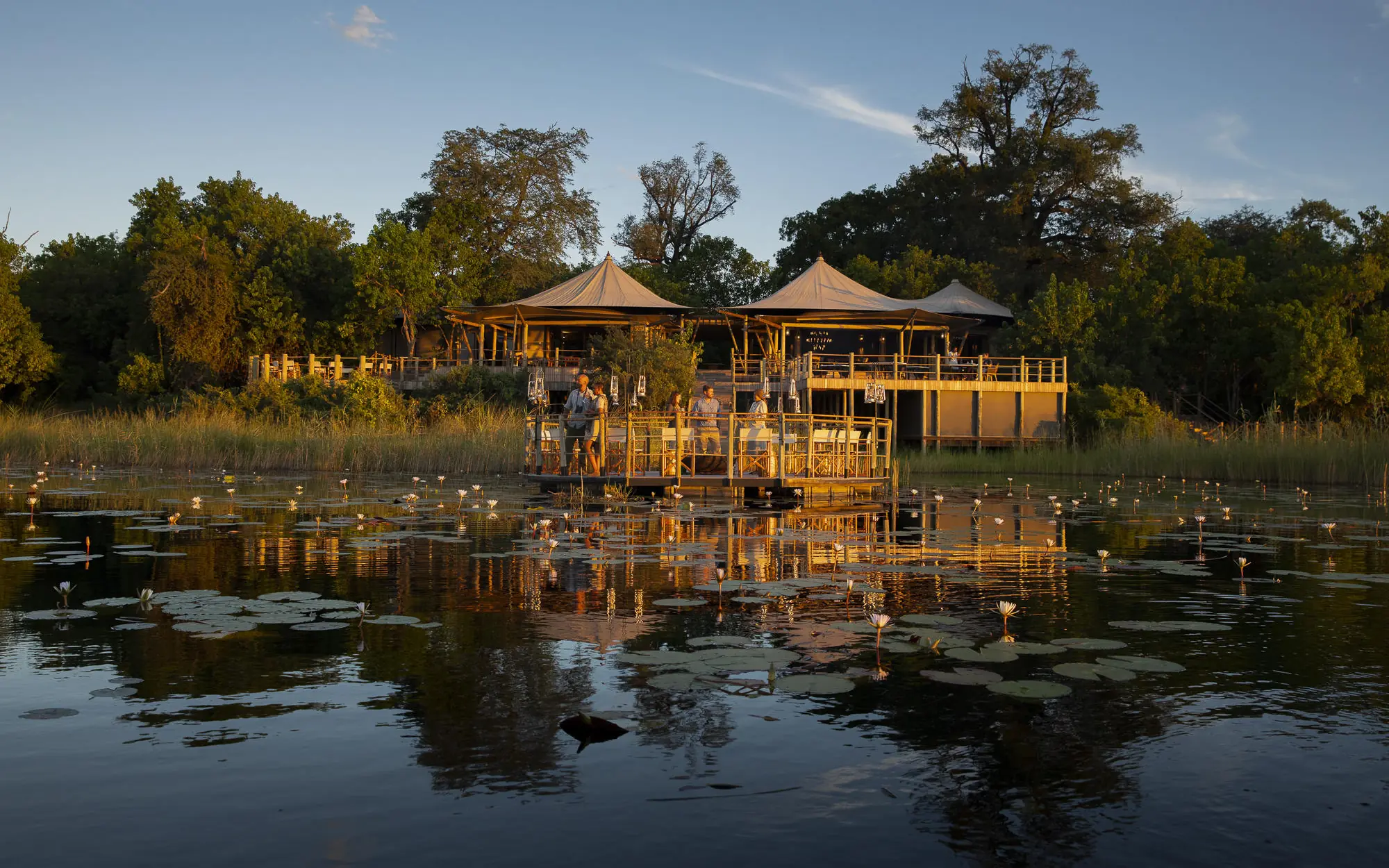 Waterfront lodge with thatched structures reflected in water, DumaTau, Linyanti Wildlife Reserve, Botswana