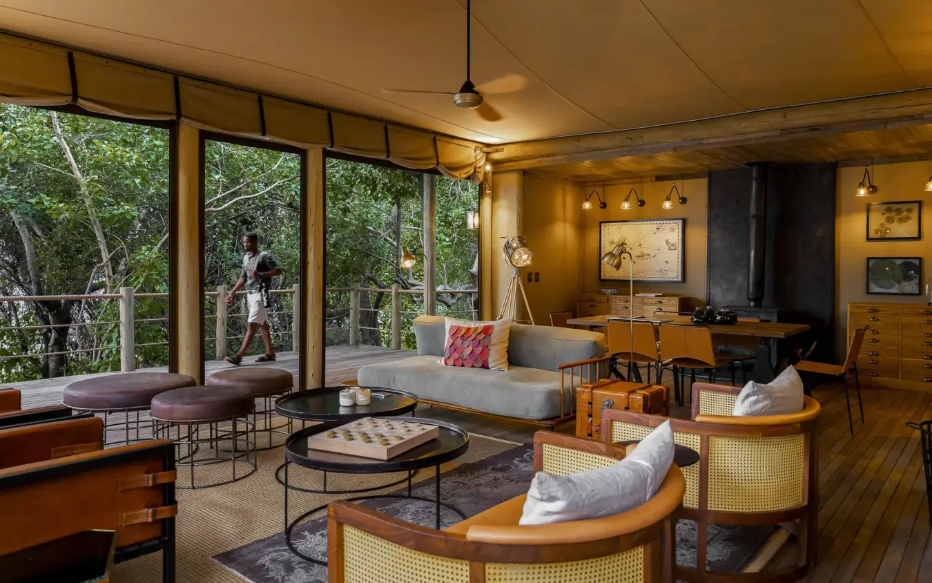 Open-plan lounge with floor-to-ceiling windows overlooking forest, DumaTau, Linyanti Wildlife Reserve, Botswana