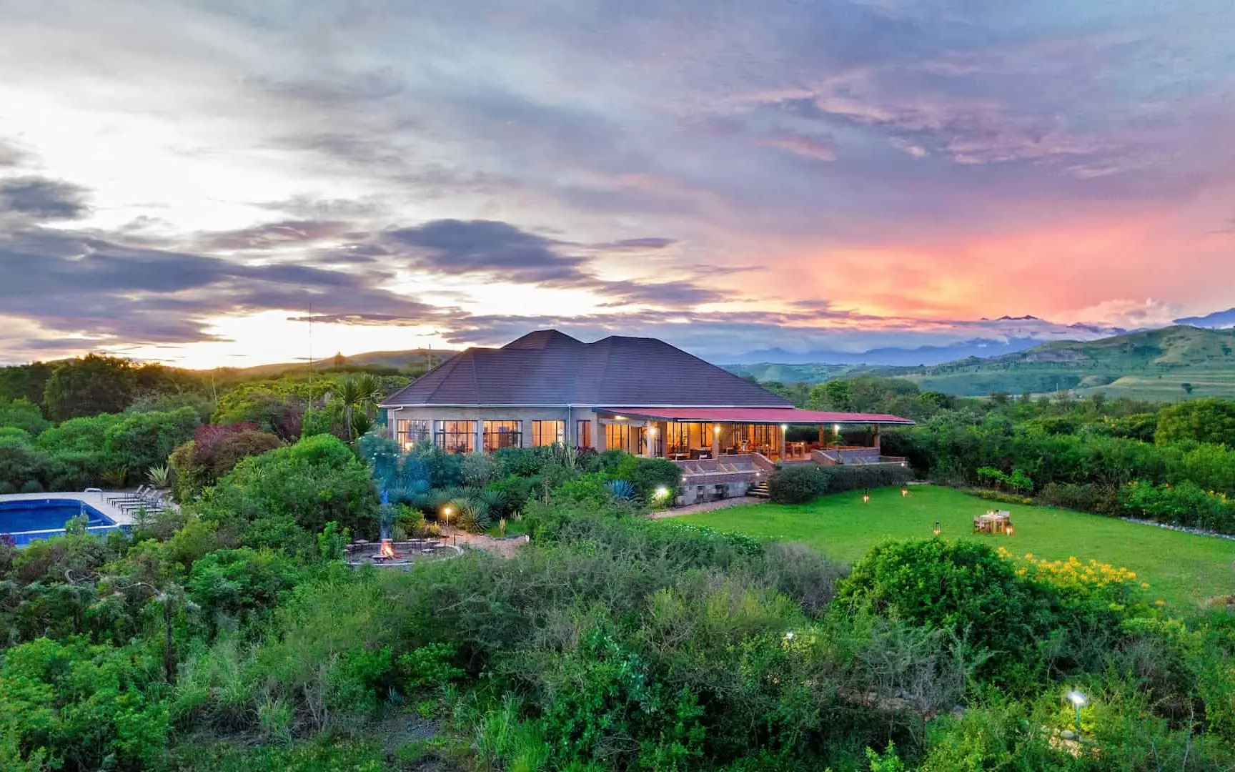 Modern lodge building illuminated at dusk with expansive green grounds, Elephant Plains Lodge, Queen Elizabeth NP, Uganda