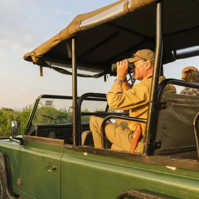 Safari guide with binoculars scanning landscape from open vehicle, Honey Bear Bush Camp, Queen Elizabeth NP, Uganda