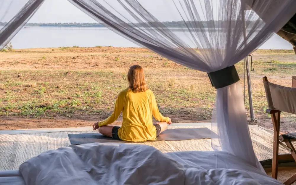 Woman meditating on deck overlooking savanna and water, Honey Bear Bush Camp, Queen Elizabeth NP, Uganda