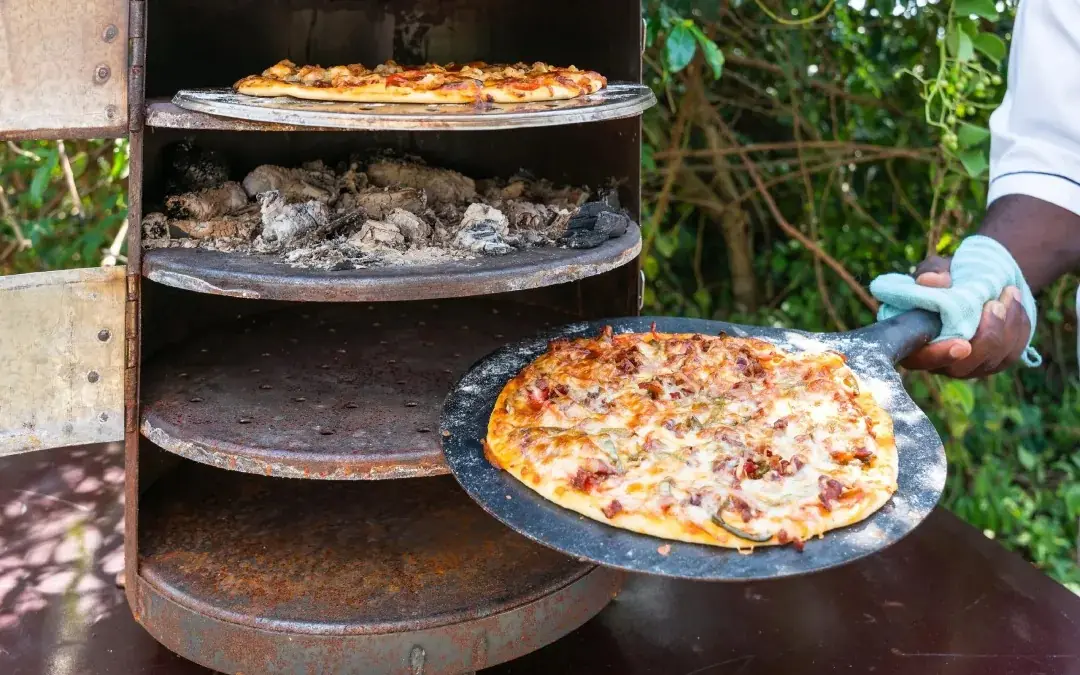Wood-fired pizza oven with freshly baked pizzas on stone plates, Honey Bear Bush Camp, Queen Elizabeth NP, Uganda