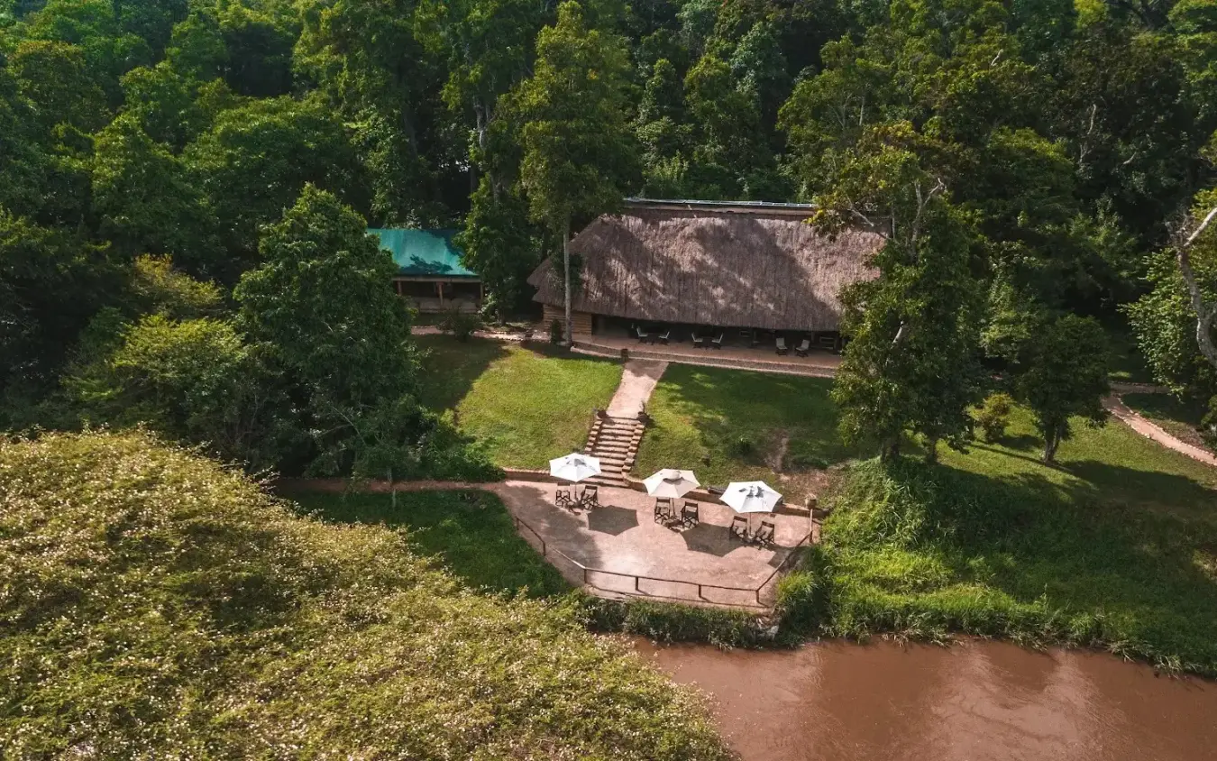 Riverside lodge with thatched roof and deck overlooking brown water, Ishasha Wilderness Camp, Queen Elizabeth NP, Uganda