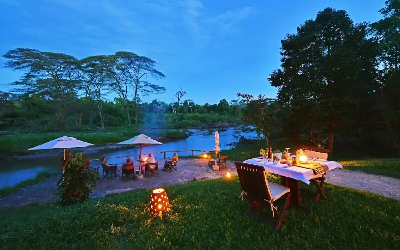 Riverside dining setup at dusk with umbrellas and seating, Ishasha Wilderness Camp, Queen Elizabeth NP, Uganda