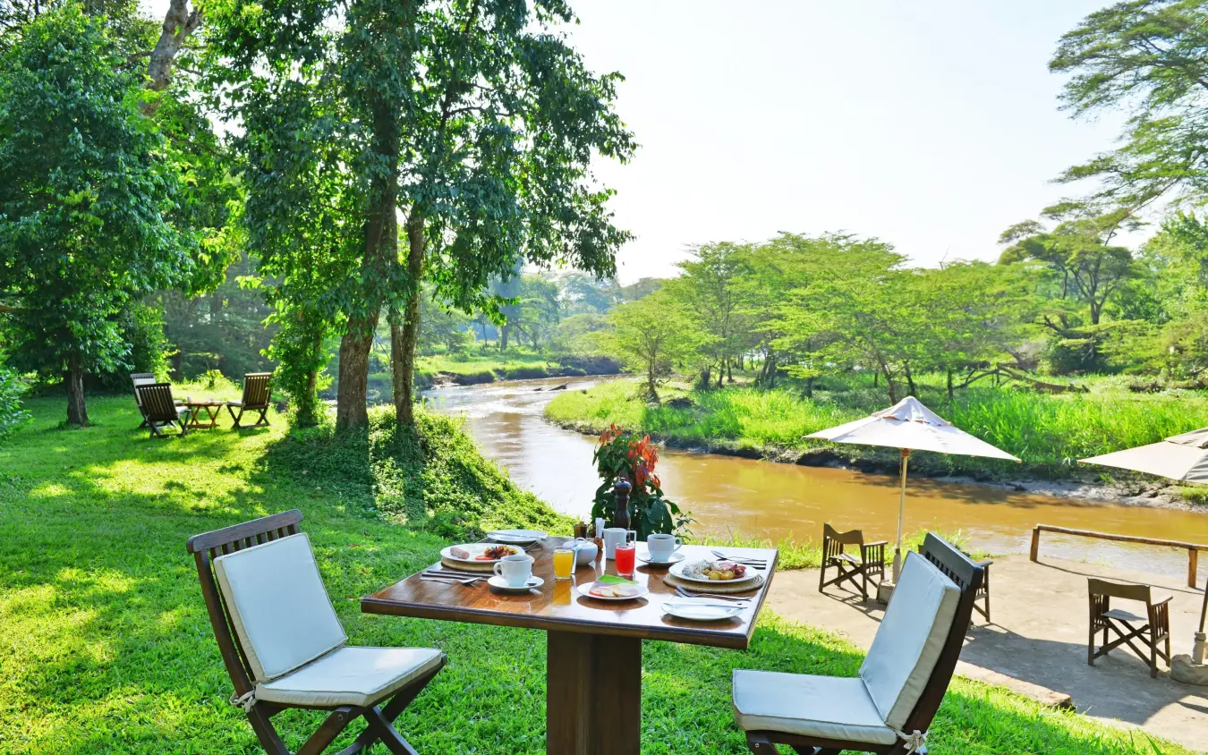 Riverside dining setup with green lawn and trees, Ishasha Wilderness Camp, Queen Elizabeth NP, Uganda