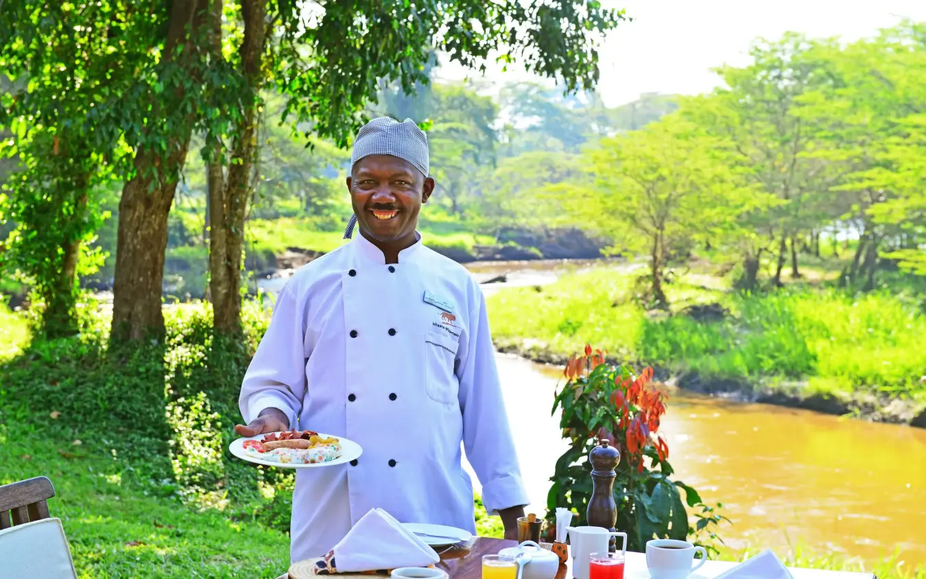 Chef presenting plated dish at riverside dining table, Ishasha Wilderness Camp, Queen Elizabeth NP, Uganda