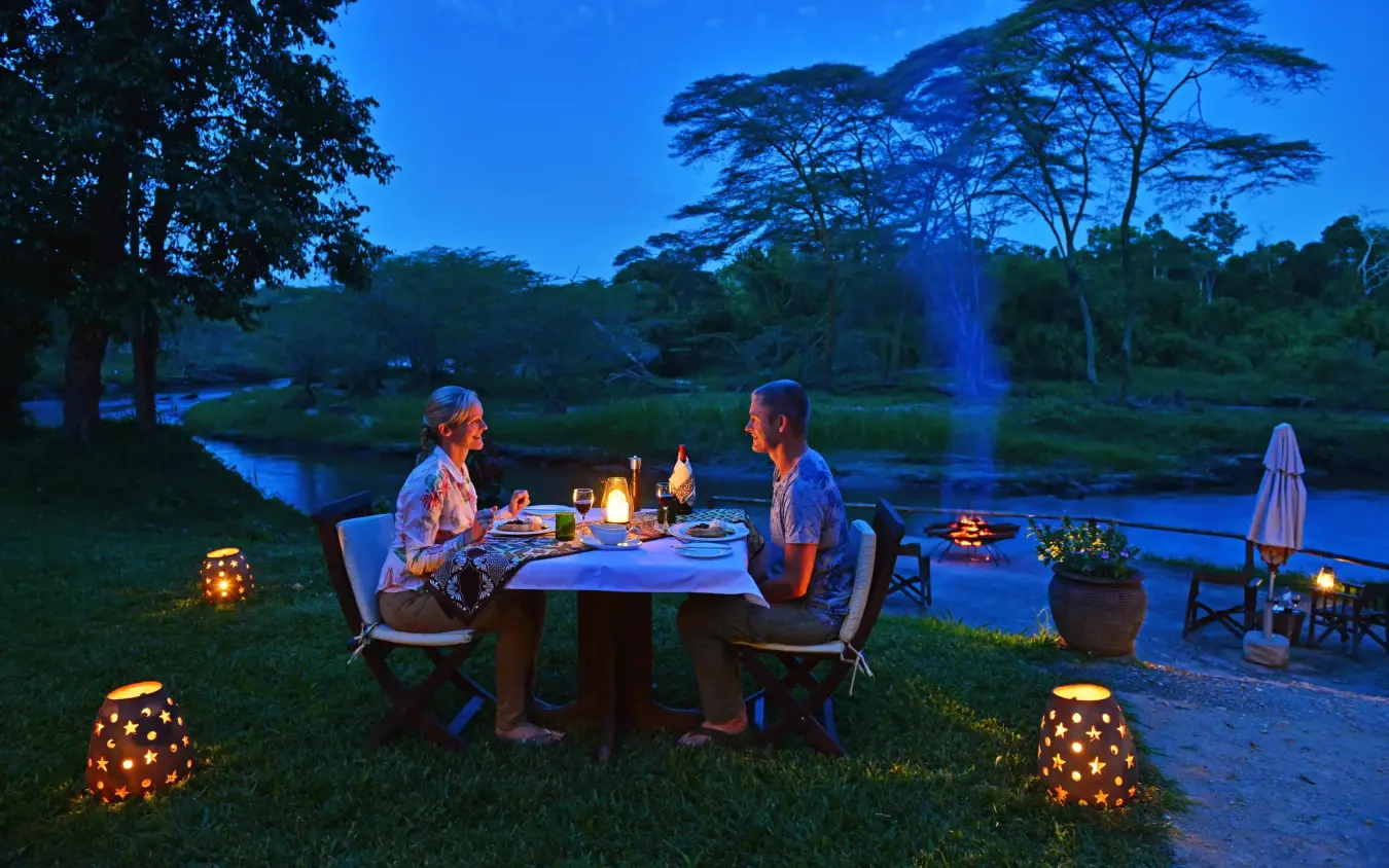 Couple dining by riverside at sunset with lantern lighting, Ishasha Wilderness Camp, Queen Elizabeth NP, Uganda
