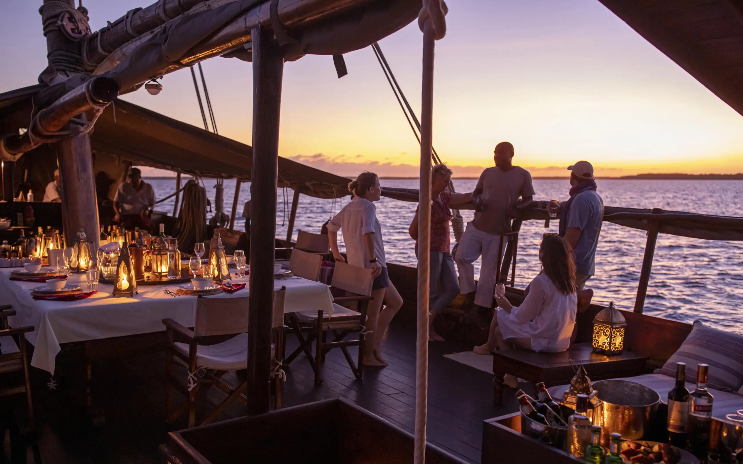 Guests dining on dhow deck at sunset over water, Tusitiri Dhow, Lamu Archipelago, Kenya