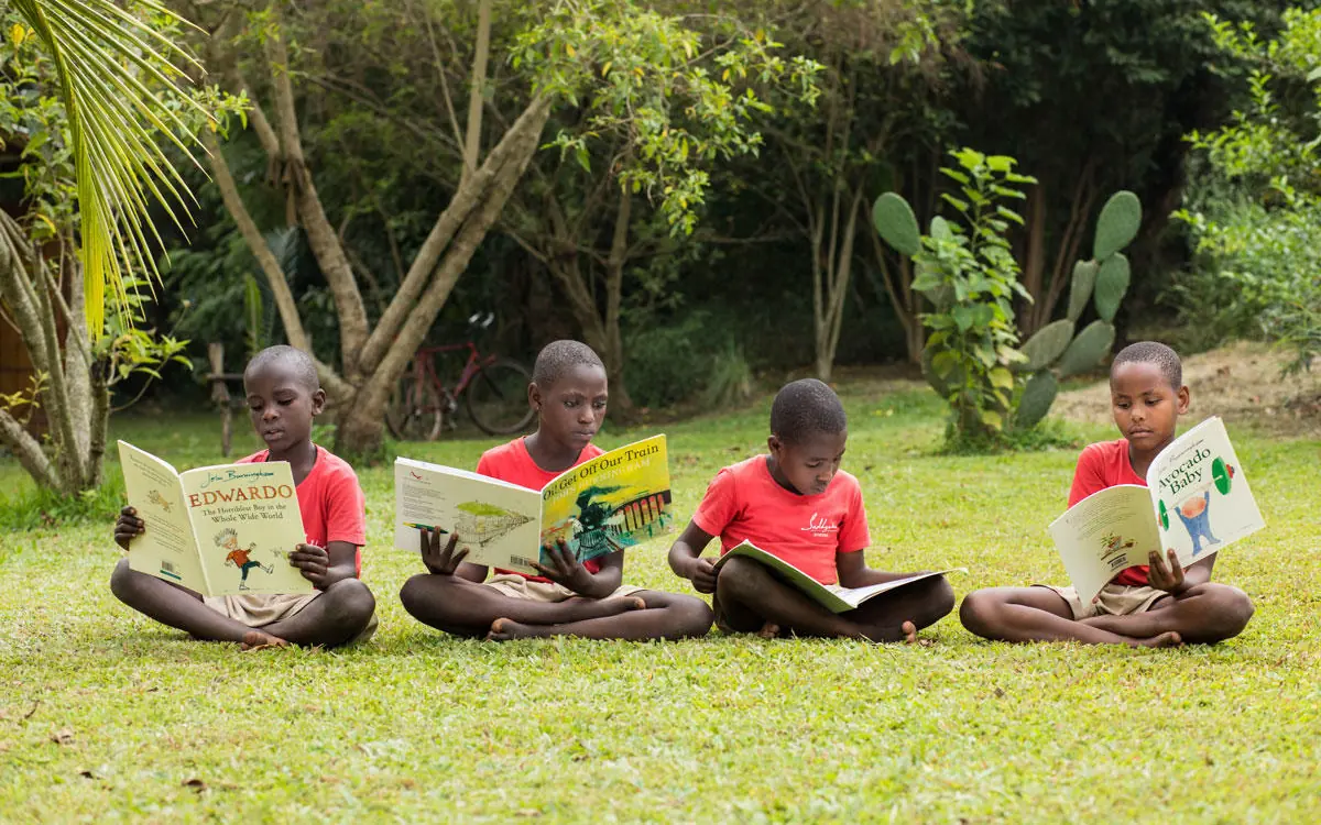 Children sitting on grass reading books outdoors, Kibale Lodge, Kibale Forest, Uganda